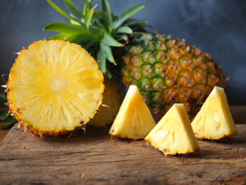 Seasonal produce - one whole and one sliced fresh pineapple fruits on a cutting board