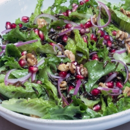 Lettuce sprinkled with walnuts, red onion and pomegranate seeds in white bowl.