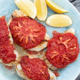 Plate of white fish with tomatoes on top