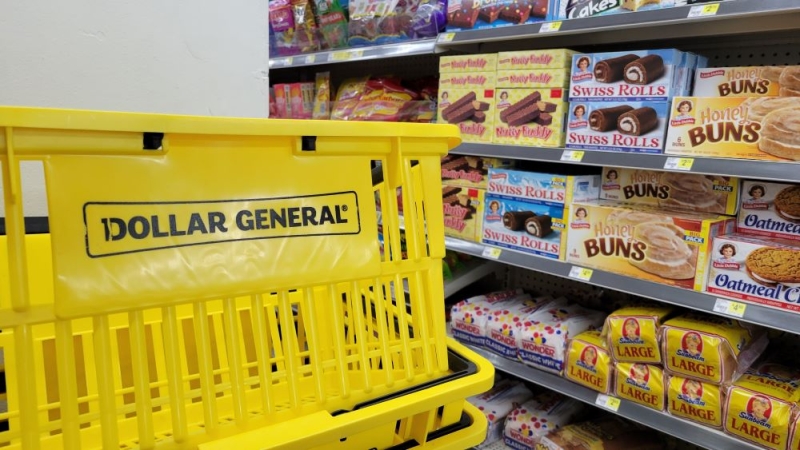 The snack aisle in a Dollar General store, with a branded yellow basket in the foreground and processed foods on the shelves