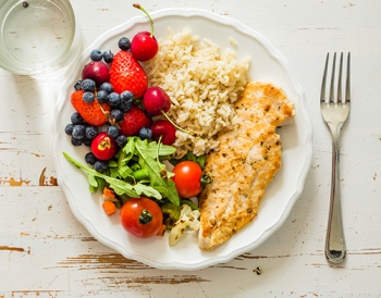 plate filled with cooked fish, leafy greens, rice and berries