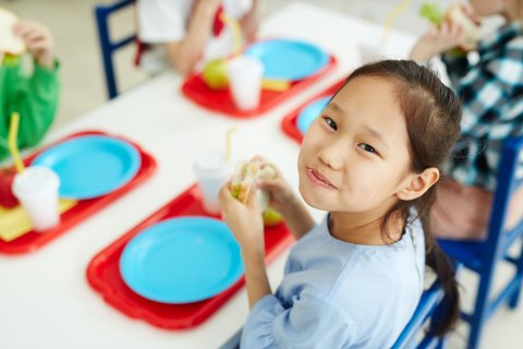 A grade-school child looks up from her school lunch tray