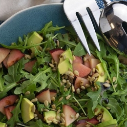 salad with greens, nectarine, avocado, sunflower seeds in blue bowl.