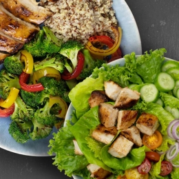 plate of chicken, vegetables, and quinoa alongside plate of chicken salad