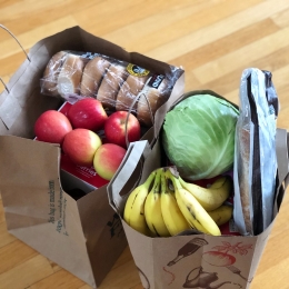 Two paper grocery bags full of apples, bananas, cabbage, and bread products