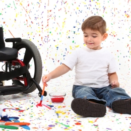 Child sitting on the floor next to wheelchair and playing with paint