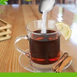 clear mug holding tea pouring sugar into
