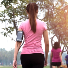 woman in a pink shirt walking away from  the camera and waring a phone holder on her arm