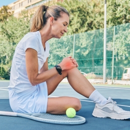 woman sitting on tennis court holding her knee