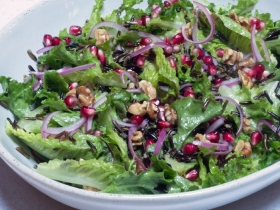 Lettuce sprinkled with walnuts, red onion and pomegranate seeds in white bowl.