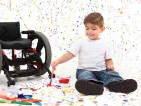 Child sitting on the floor next to wheelchair and playing with paint