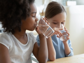 2 young girls drinking water out of clear glasses