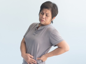 woman in grey shirt holding her hip and wincing in pain