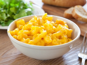 Bowl of macaroni and cheese with bread and salad in background