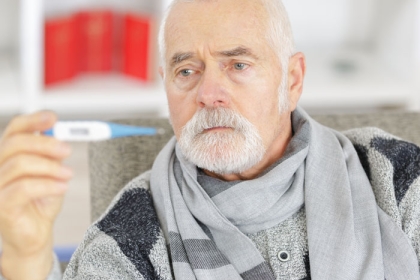 older man in scarf looking at thermometer