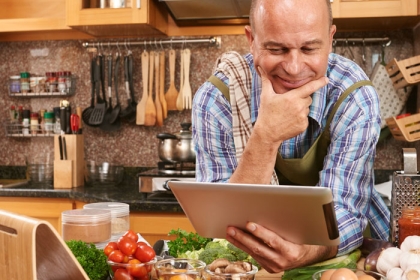 man in kitchen looking at ipad with lots of vegetables on the counter