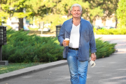 older man walking down street with coffee and paper