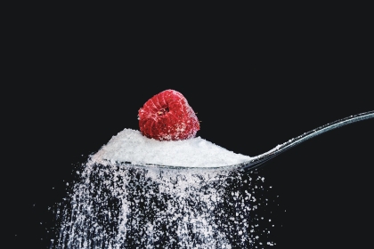 A spoonful of white cane sugar with a raspberry on top