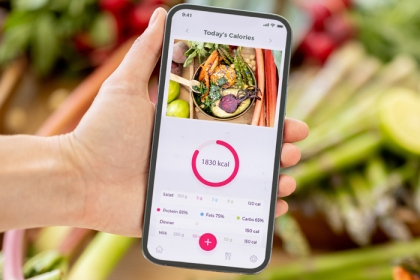 hand holding a phone with food tracker on the screen and vegetables in background