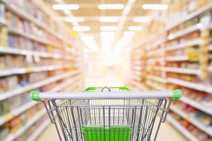 Supermarket aisle product shelves interior blur background with empty shopping cart