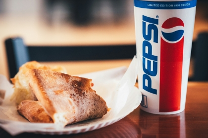A slice of pizza on a paper plate and a fountain soda in a Pepsi cup