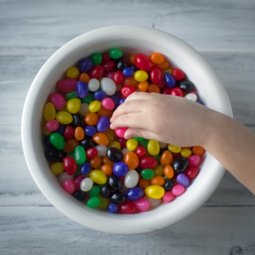 Child reaching into a bowl of brightly colored jelly beans