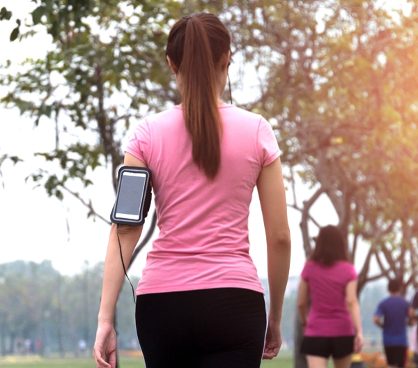 woman in a pink shirt walking away from  the camera and waring a phone holder on her arm