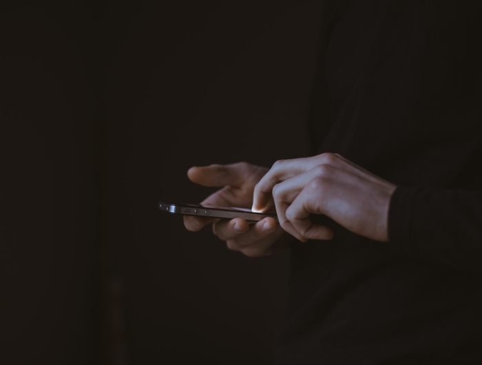A pair of hands holding an iPhone looms out of an otherwise dark image.