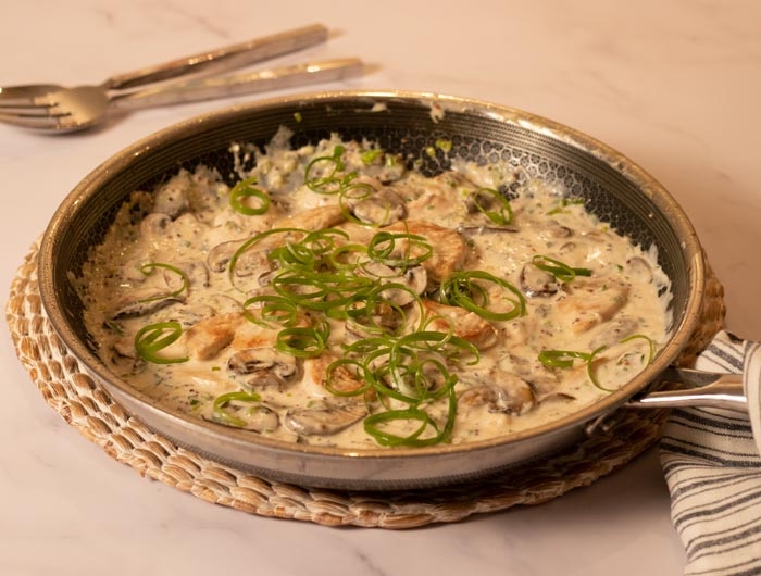 large pan filled with chicken, mushrooms, creamy sauce and topped with green scallion strips
