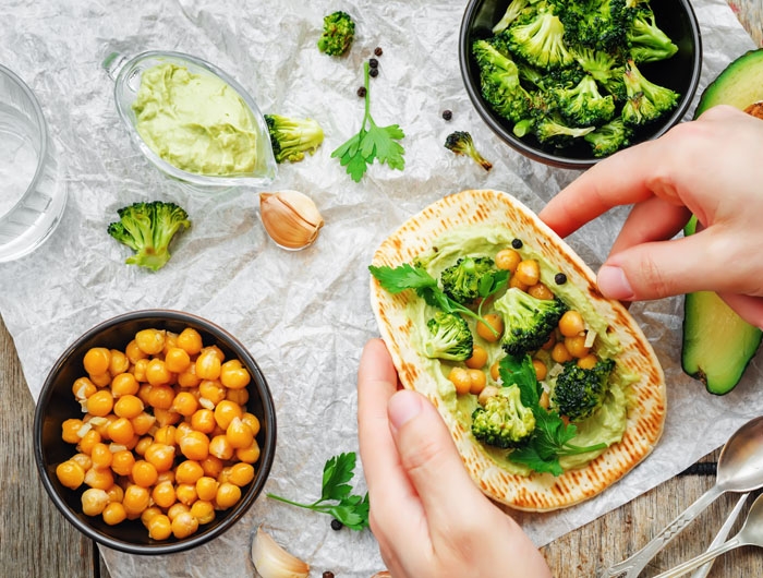 bowl of broccoli, bowl of chickpeas, hands making a pita with broccoli and chickpeas
