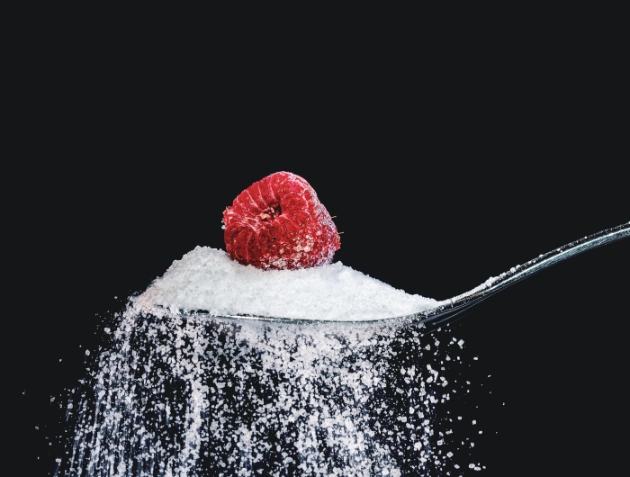 A spoonful of white cane sugar with a raspberry on top