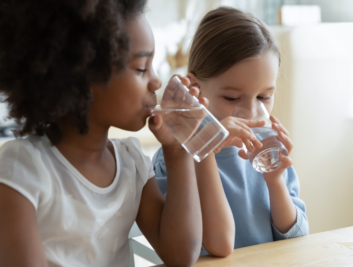 2 young girls drinking water out of clear glasses