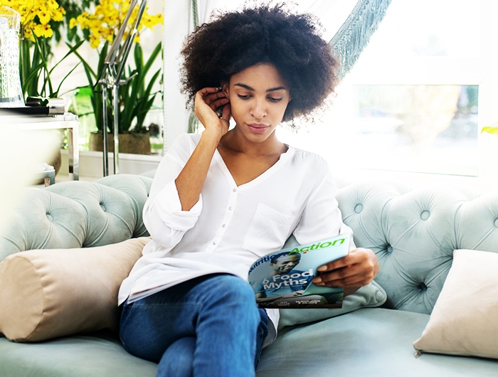 woman sitting on a couch and reading a Nutrition Action magazine