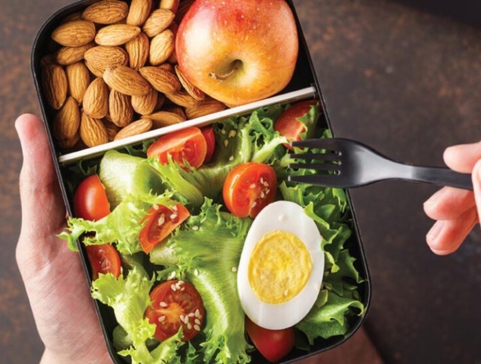 box of food with a salad, egg, almonds, and apple