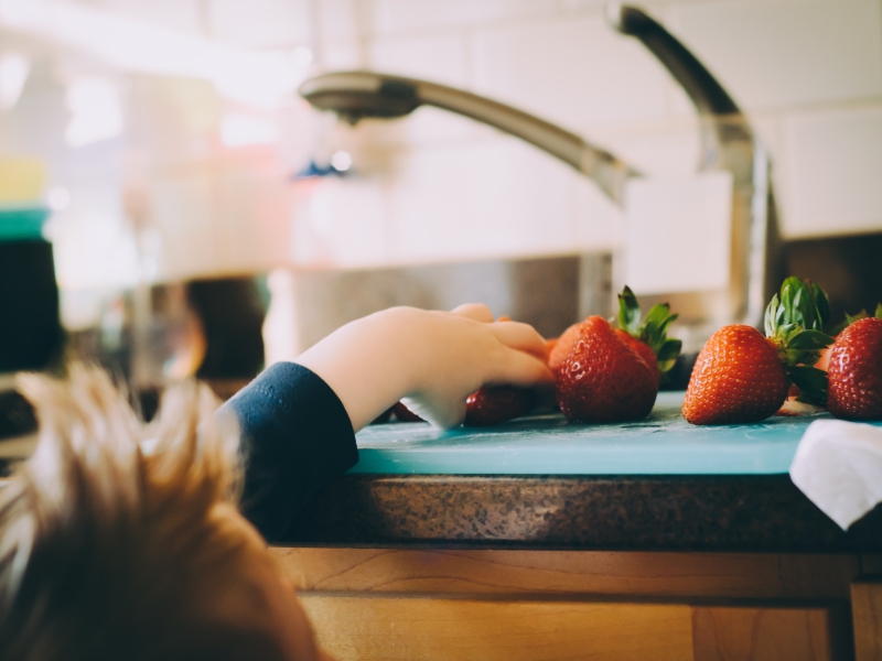 A child reaching for strawberries on the counter
