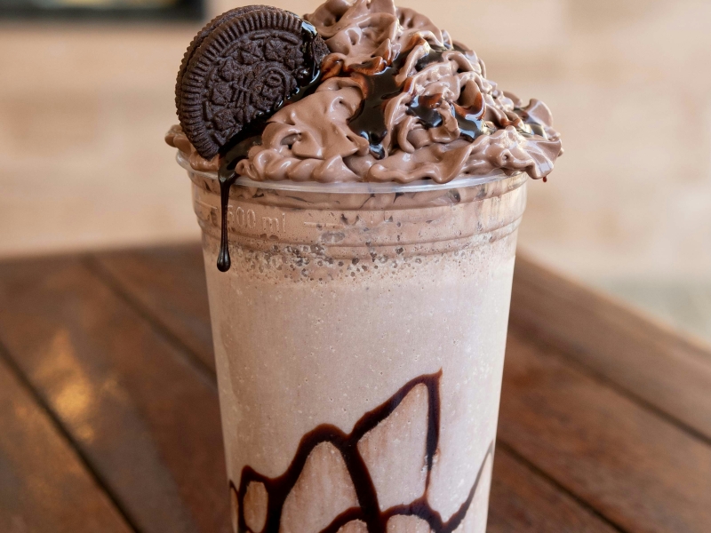 A large milkshake with cookies and chocolate syrup in a to-go cup