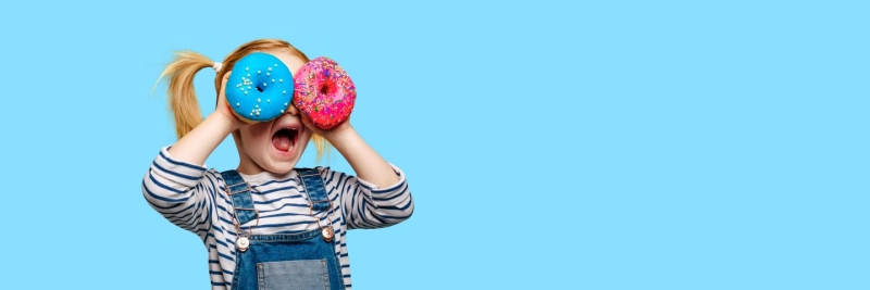 A girl holds two colorful donuts over her eyes with a blue background