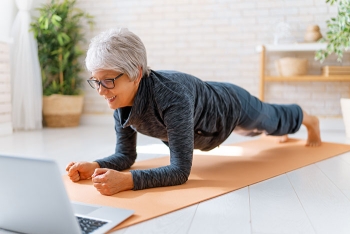 woman doing exercise plank while looking at a laptop computer