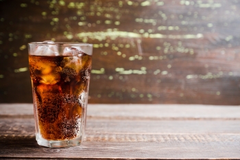 clear glass of cola on ice on wood table in the sun