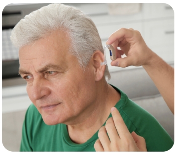 older man having a hearing aid placed on his ear