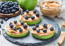 Plate with green apple slices covered in peanut butter and sprinkled with blueberries